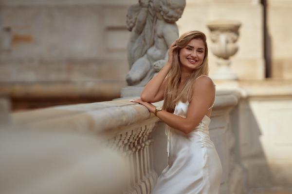 Modelka w białej satynowej sukni opierająca się o kamienną balustradę pałacu – matee.photo
