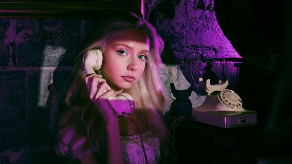 Kobieta rozmawia przez retro telefon z tarczą przy różowo-fioletowym neonowym świetle, koronkowa sukienka, figurka kota – matee.photo