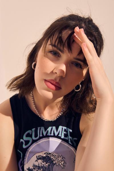 Kobieta w czarnym topie z napisem SUMMER i falą, dłoń unosi grzywkę, srebrny łańcuszek na szyi – matee.photo
