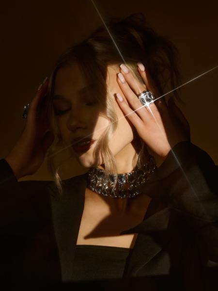 Zbliżenie dłoni z kryształowym pierścieniem przy twarzy modelki, promień światła przecinający kadr, choker na szyi – matee.photo
