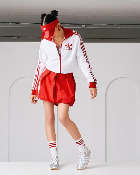 Kobieta w białej bluzie adidas z czerwonymi lampasami i bufiastej czerwonej spódnicy, dwa kucyki, srebrne sneakersy – matee.photo