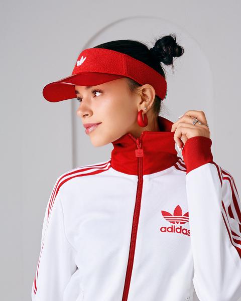 Zbliżenie na twarz w czerwonym daszku adidas i biało-czerwonej bluzie sportowej, kolczyki kółka, dłoń przy kołnierzu – matee.photo