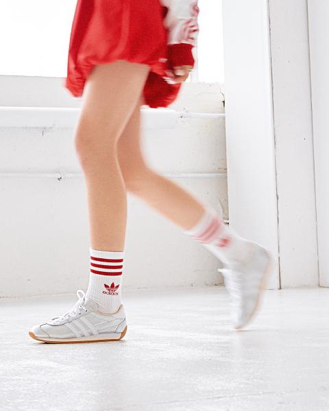 Zamazane w ruchu nogi w białych skarpetach z czerwonymi paskami i srebrnych sneakersach adidas, czerwona spódnica – matee.photo