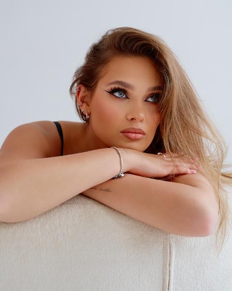 Jasne wnętrze, portret kobiety opartej łokciami o biały fotel – matee.photo