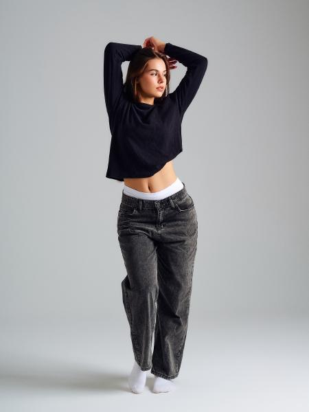 Modelka w czarnej krótkiej bluzce i szarych jeansach typu baggy, ręce nad głową, białe skarpetki – matee.photo
