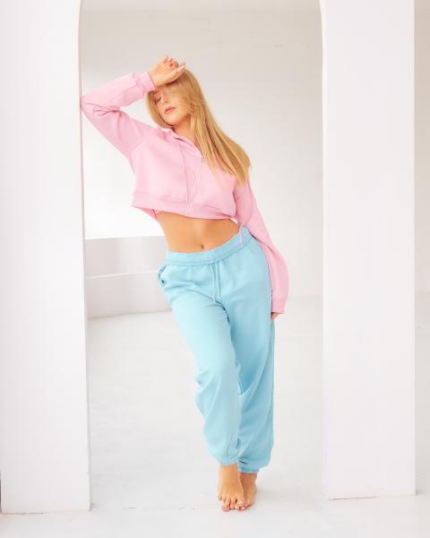 Blond modelka w różowej bluzie crop i błękitnych spodniach dresowych, poza w białym wnęku – matee.photo